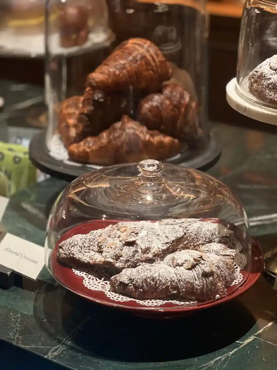 Artisan almond and chocolate pastries under glass cloches in an understated patisserie setting