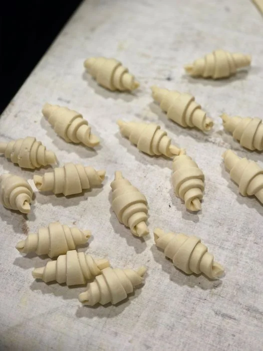 Raw unbaked croissants rolled and arranged meticulously on floured surface prior to proving